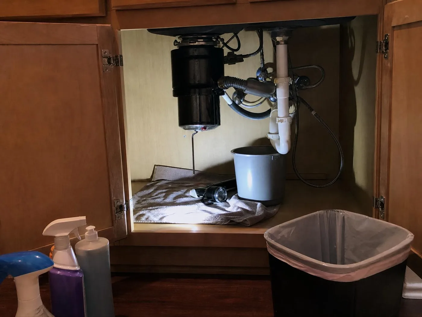 Open cabinet under a kitchen sink with a garbage disposal, an Allen wrench in the reset socket, towel, bucket and flashlight (illustration)