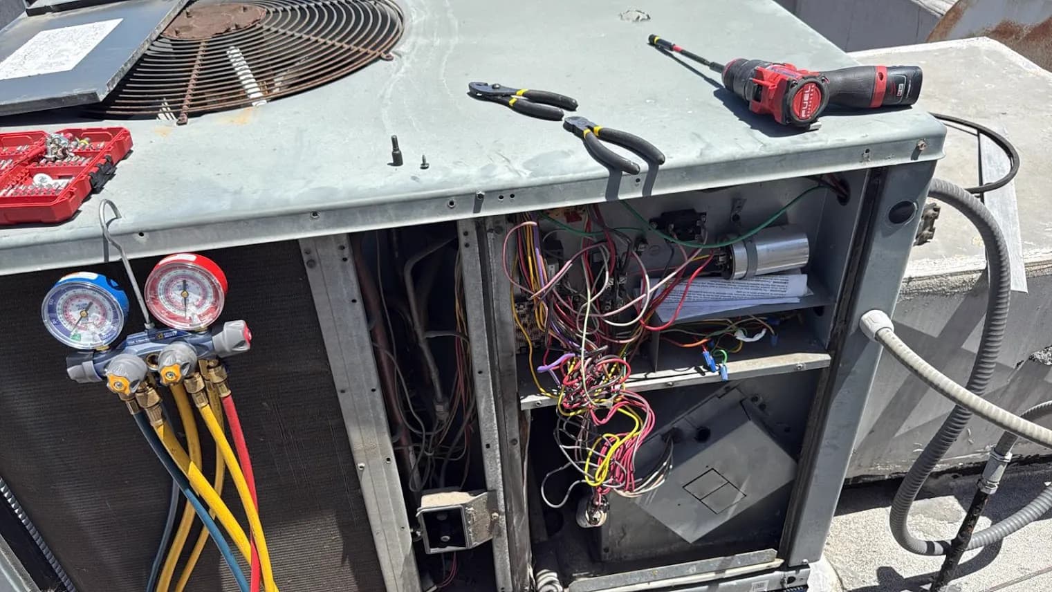 Rooftop AC package unit opened up, manifold gauges connected and wiring exposed