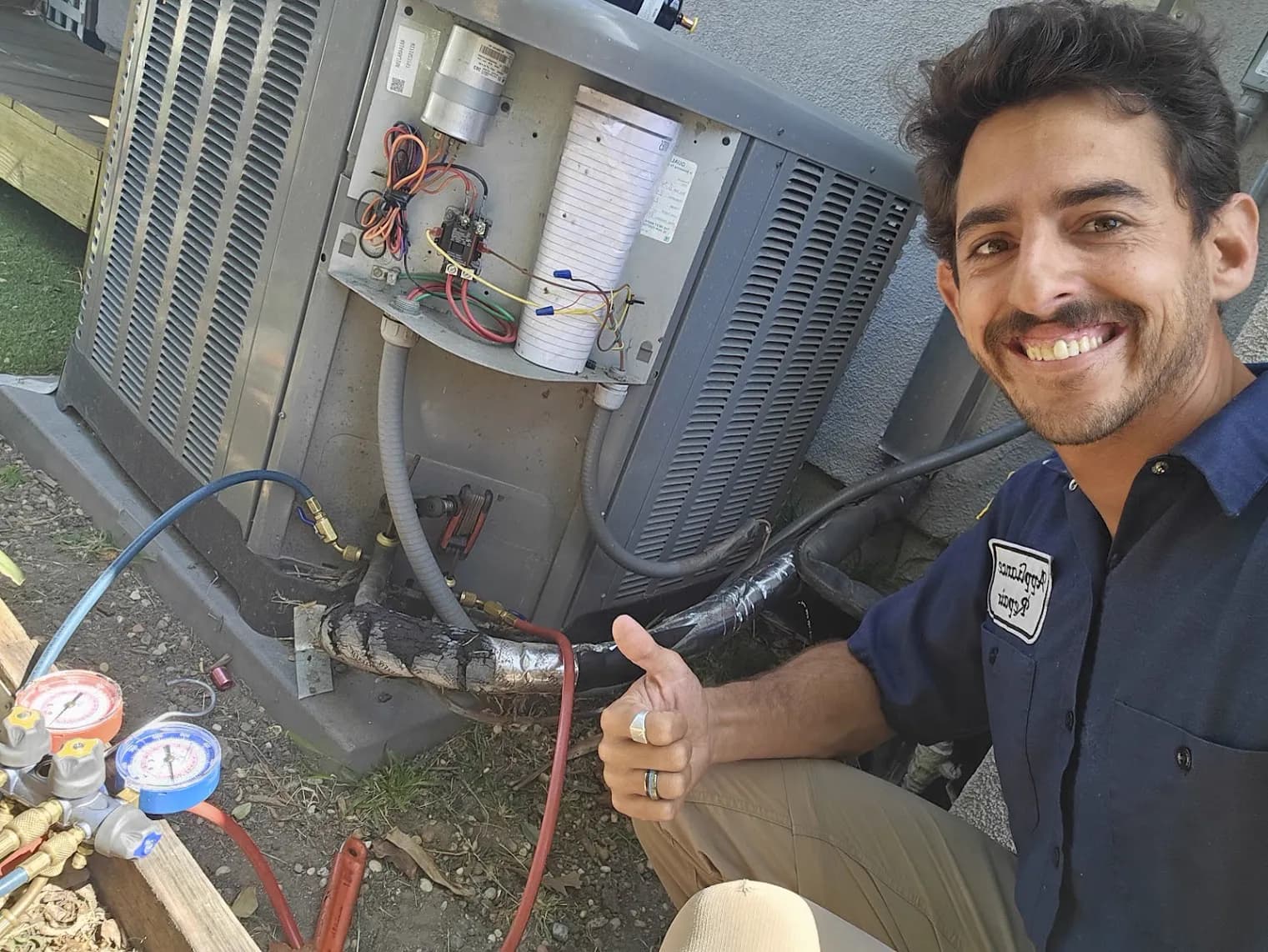 Technician giving a thumbs-up beside an outdoor AC condenser with gauges connected
