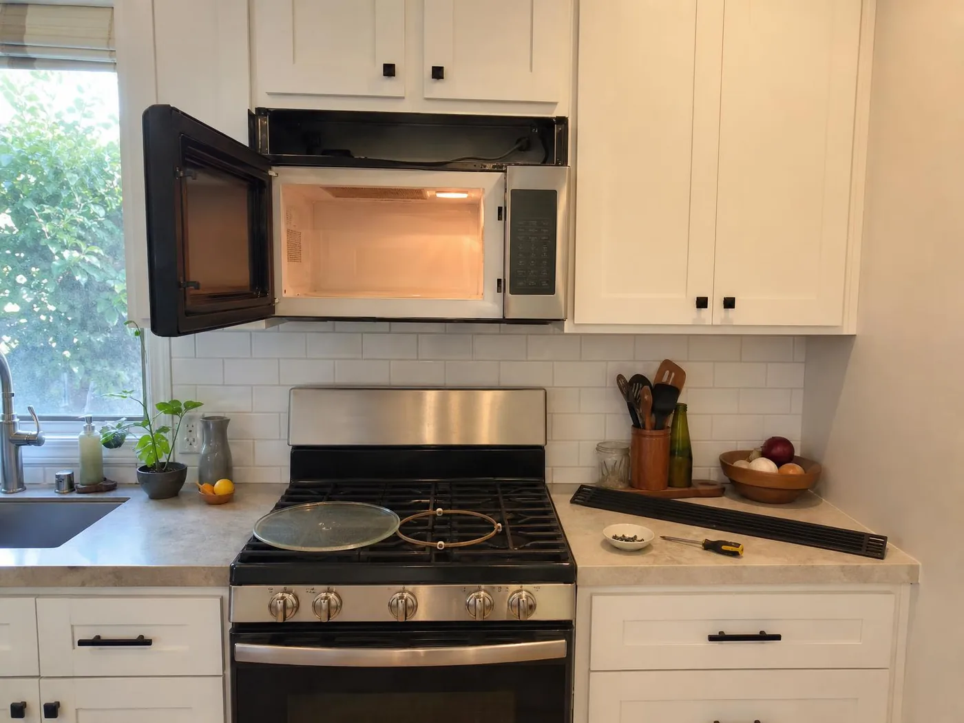 Over-the-range microwave with the door open and the vent grille removed, turntable resting on the range below (illustration)