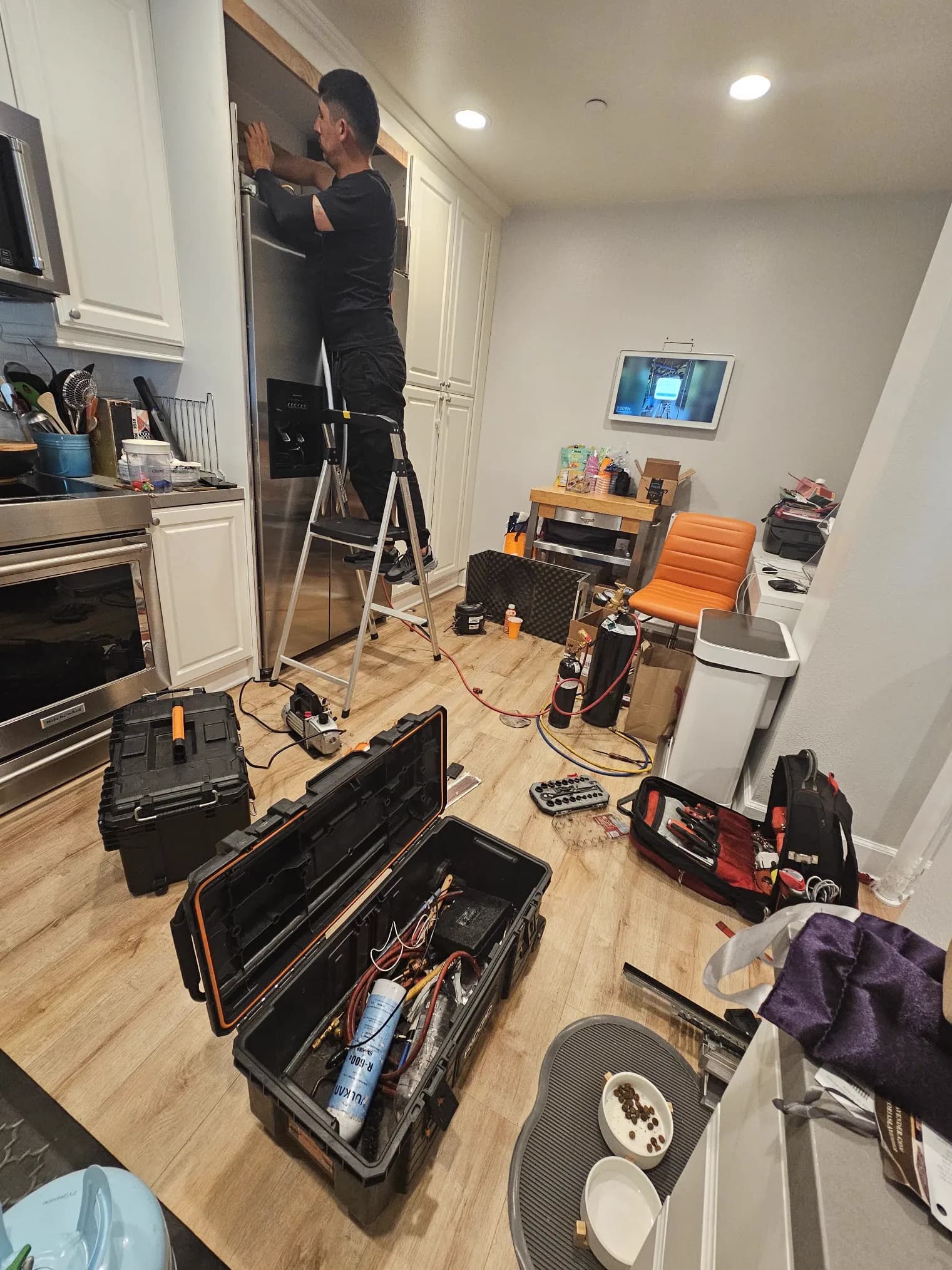 Technician on a ladder working on a built-in refrigerator in a customer's kitchen